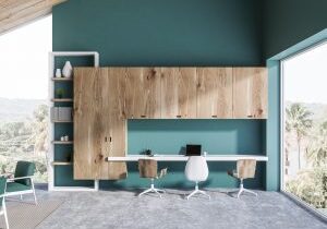 Home office interior with blue green walls, concrete floor, white computer table with a laptop on it and white bookcase. 3d rendering
